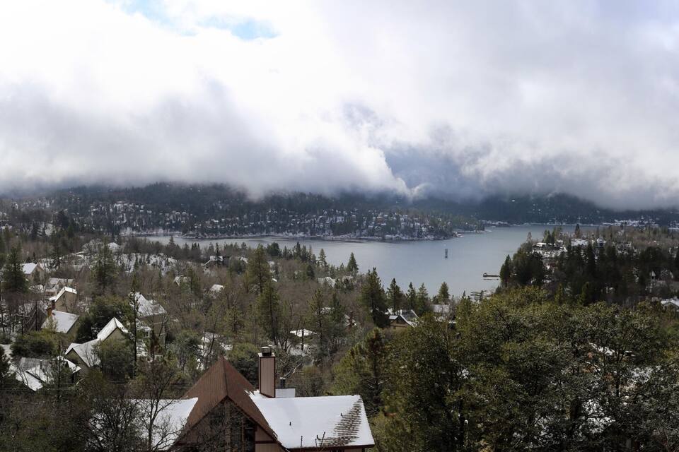 Un paisaje montañoso con un lago, casas y bosque denso.