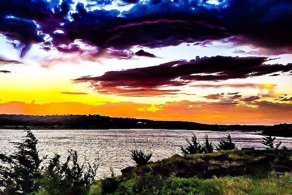 A sunset over a body of water with a silhouette of land in the distance.