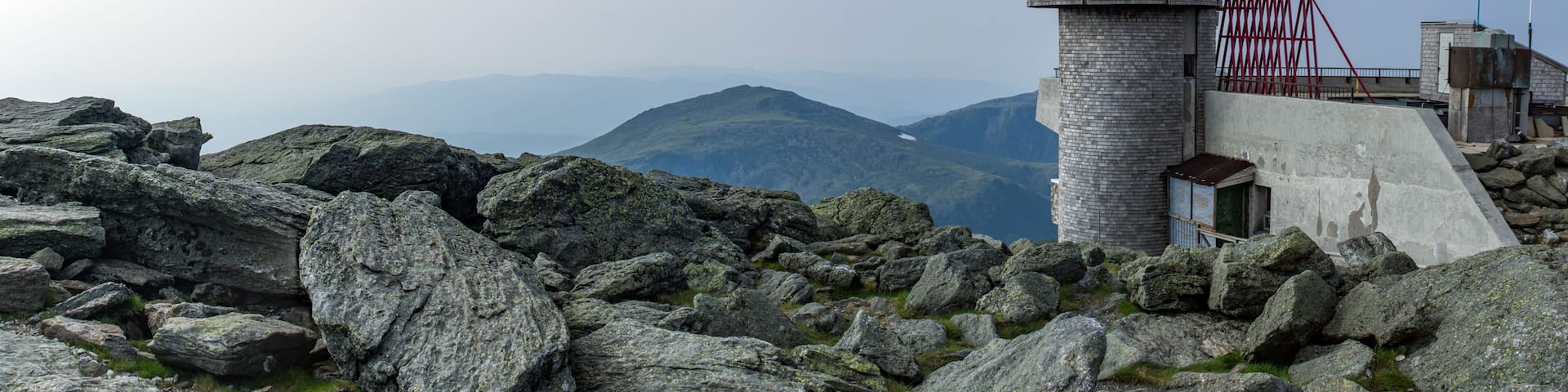 A stone lighthouse on a rocky outcrop with a clear sky and mountains in the background.