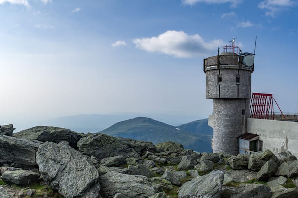 A stone lighthouse on a rocky outcrop with a clear sky and mountains in the background.