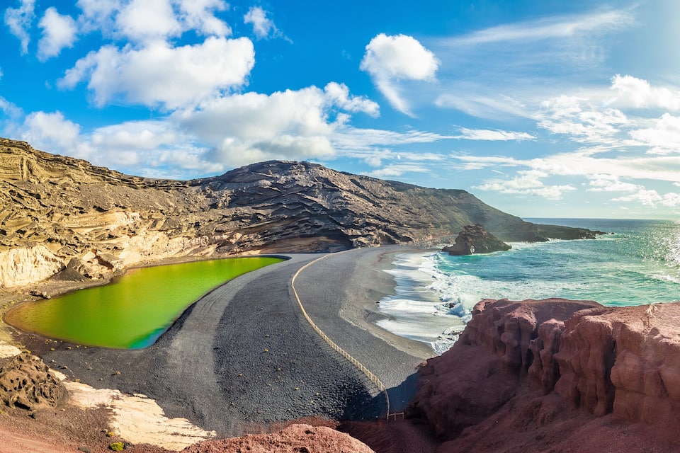 Paisagem costeira com uma lagoa verde, uma praia de areia e falésias rochosas.