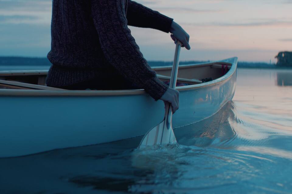 A person in a boat on calm water with a distant shoreline.
