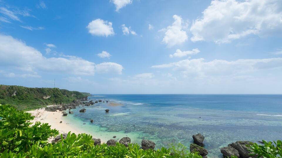 A tropical beach with clear turquoise waters, rocky outcrops, and lush greenery.