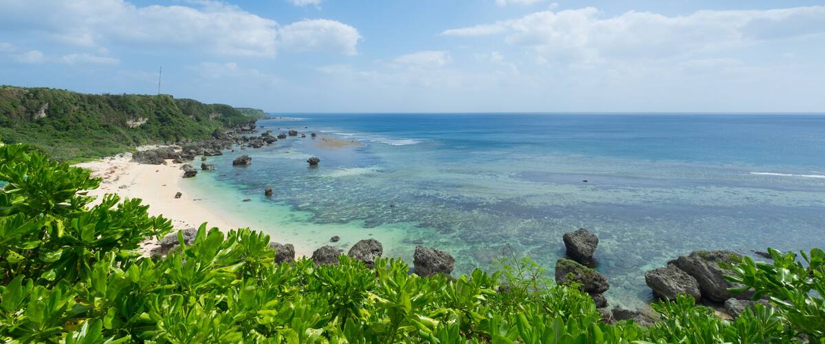 A tropical beach with clear turquoise waters, rocky outcrops, and lush greenery.