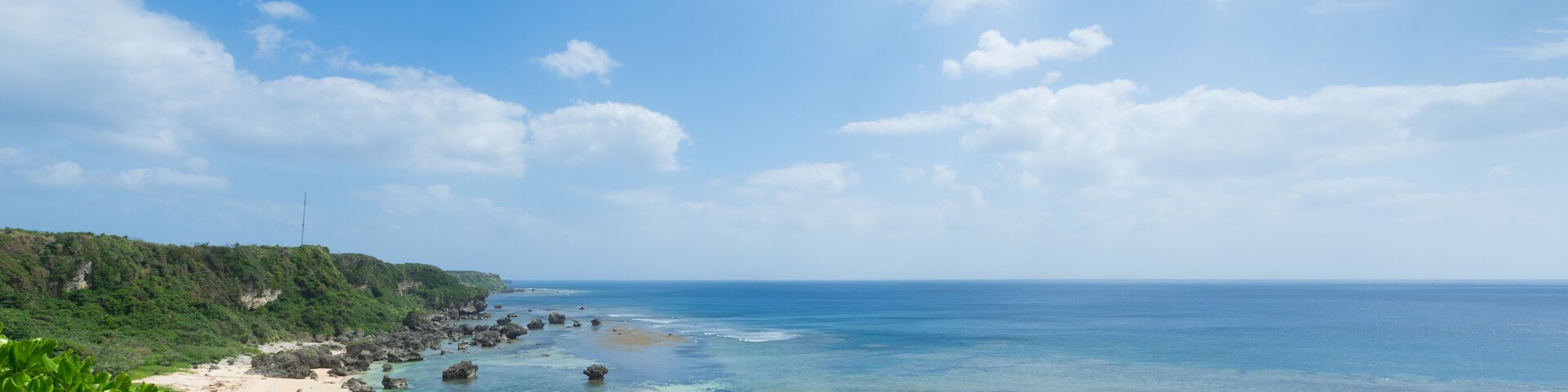 A tropical beach with clear turquoise waters, rocky outcrops, and lush greenery.