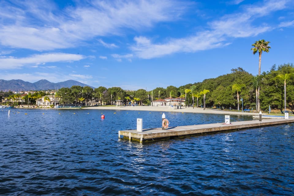 A waterfront with a dock, palm trees, and a mountainous background.
