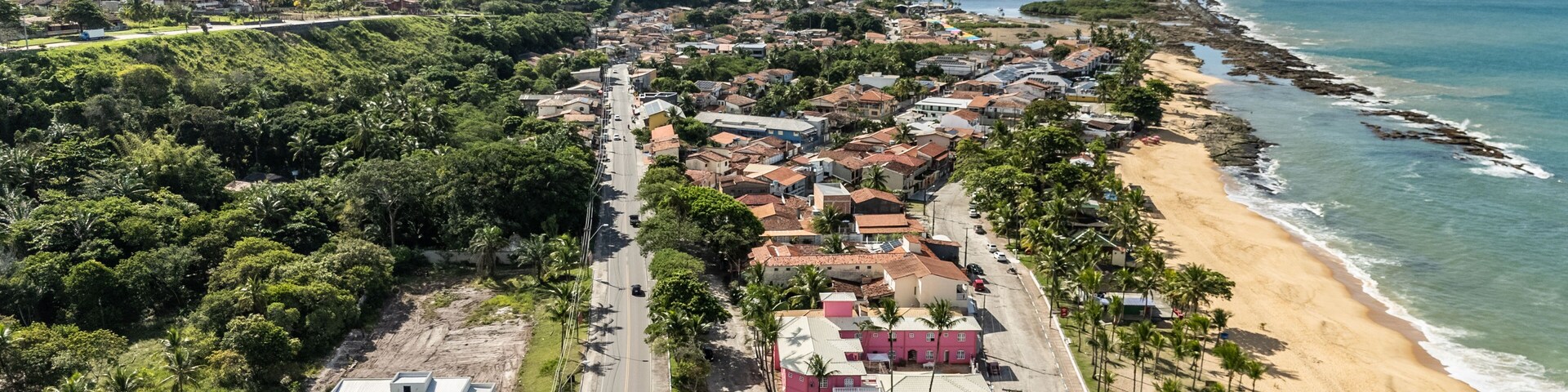 A coastal town with a beach, dense greenery, and a mix of residential and commercial buildings.