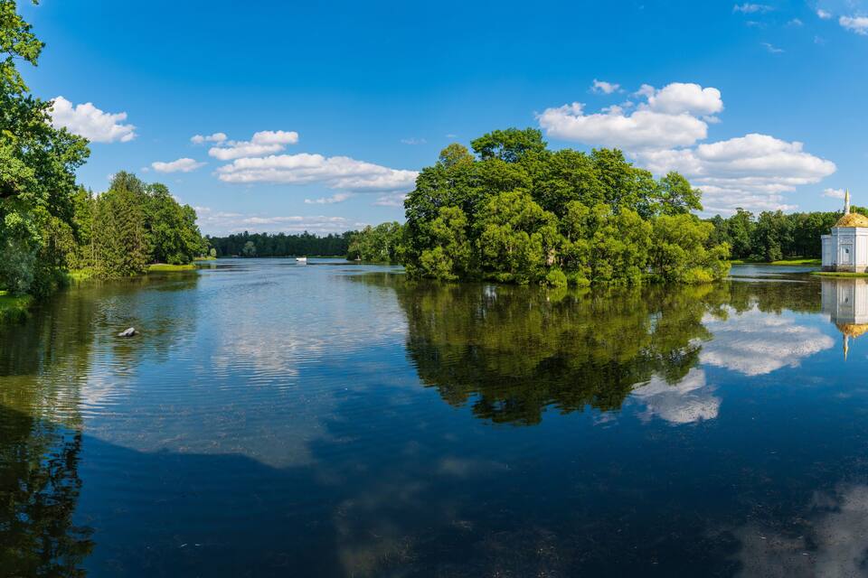 A calm lake with a small white building on the right and dense green trees on both sides.