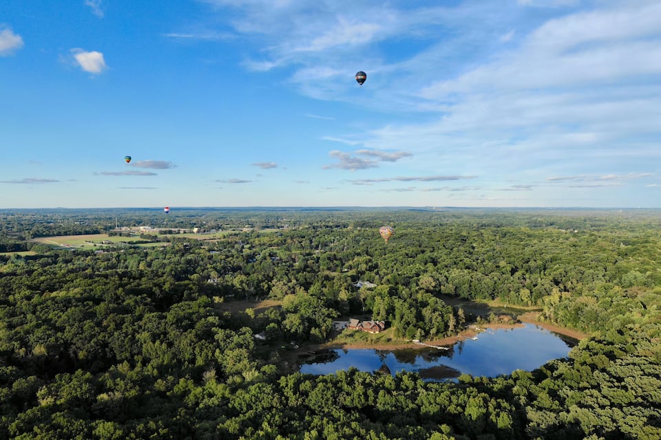 A hot air balloon over a forested area with a lake and a small house.
