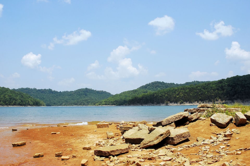 A rocky shoreline with a clear blue sky and distant green hills.