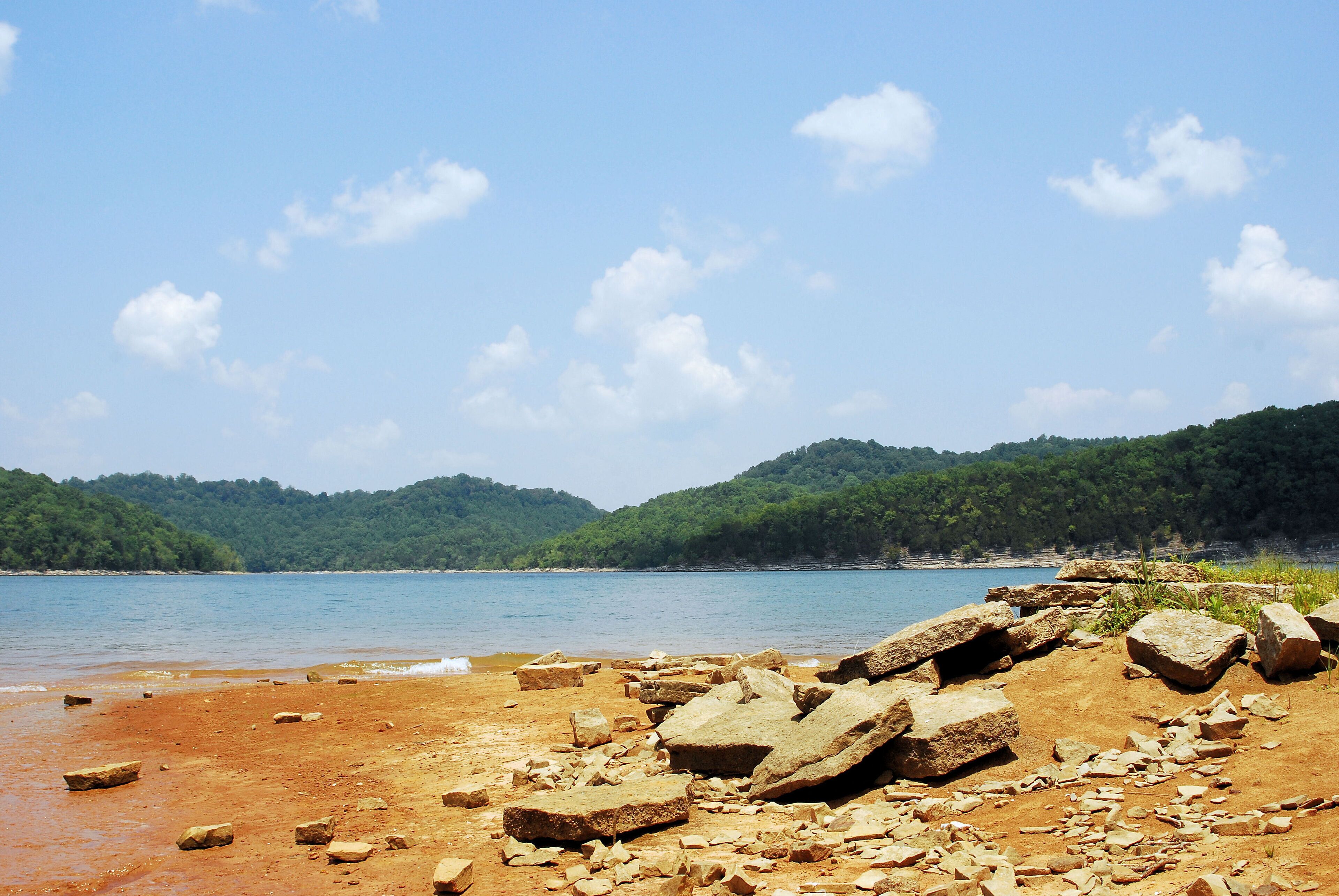A rocky shoreline with a clear blue sky and distant green hills.