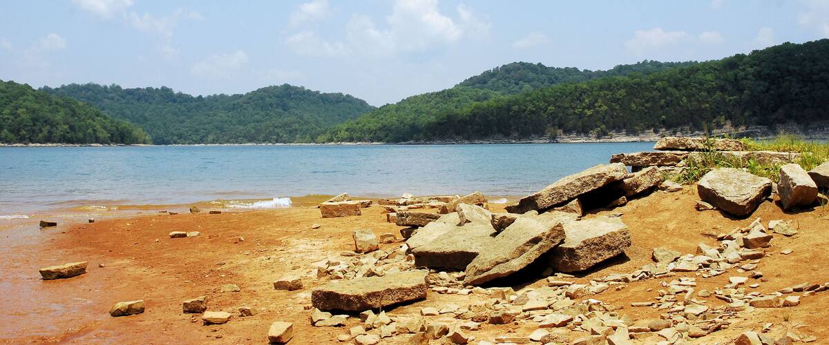 A rocky shoreline with a clear blue sky and distant green hills.