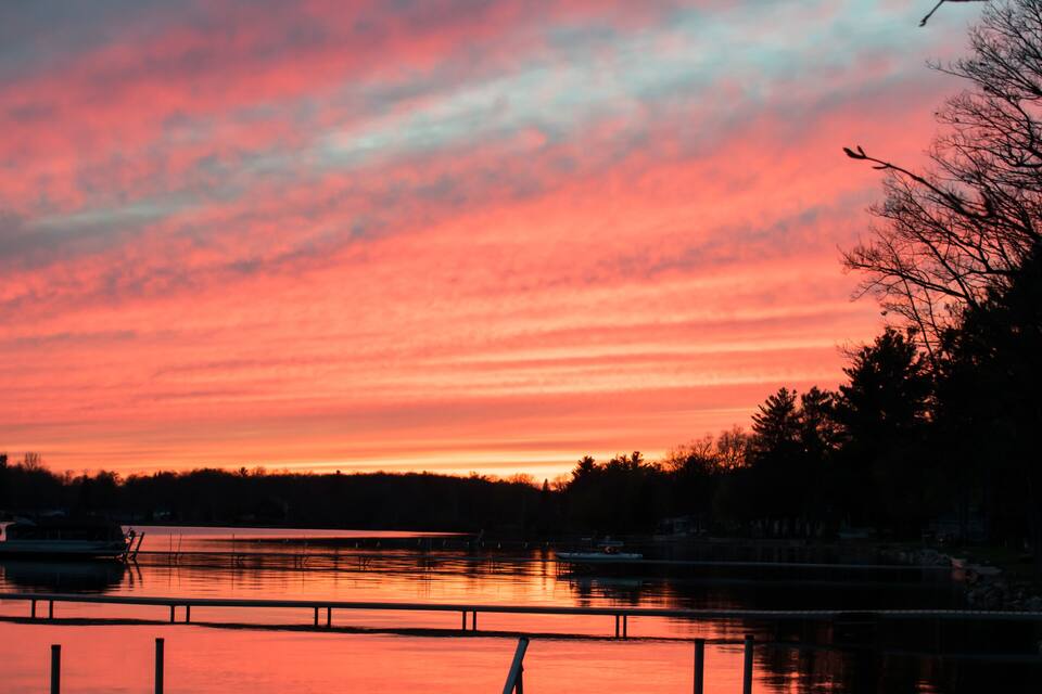 A sunset over a calm lake with a metal railing in the foreground.