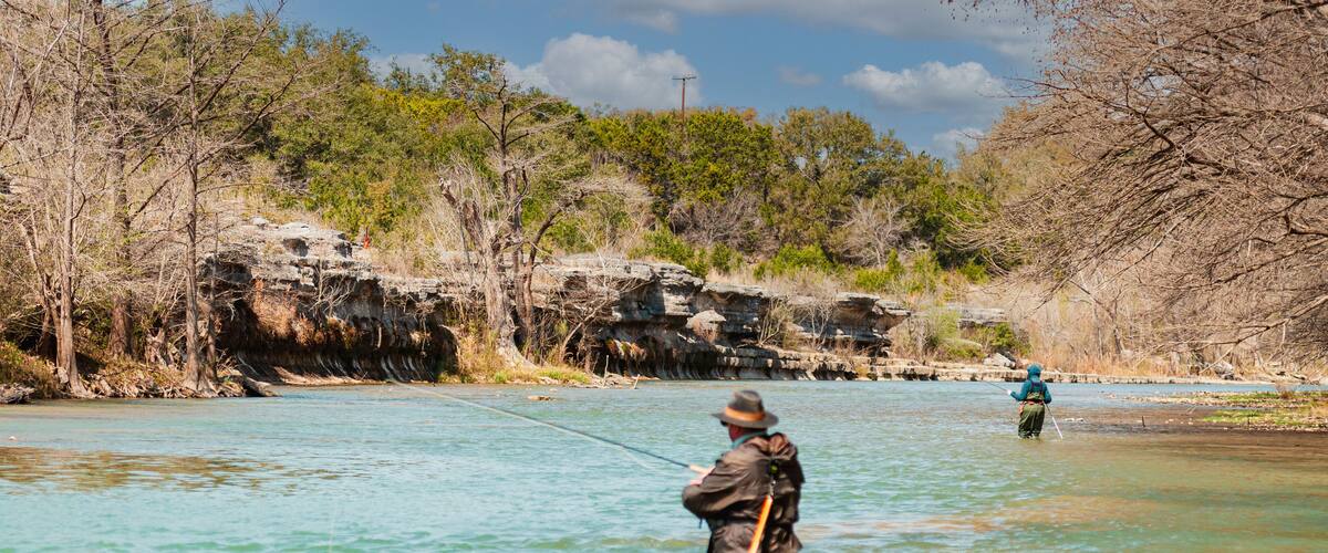 Two anglers fly fishing for trout in the Guadalupe River 5 miles below Canyon Lake Dam facing limestone outcrop in the winter sports paradise of Central Texas, USA.