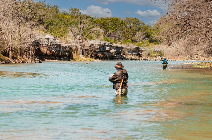 Two anglers fly fishing for trout in the Guadalupe River 5 miles below Canyon Lake Dam facing limestone outcrop in the winter sports paradise of Central Texas, USA.