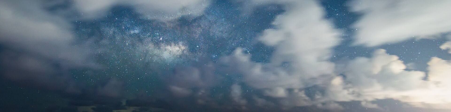 A beach with two lounge chairs, a rocky outcrop, and a starry night sky.