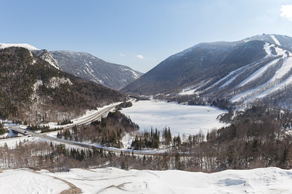 A snow-covered valley with a highway, mountains, and a frozen lake.