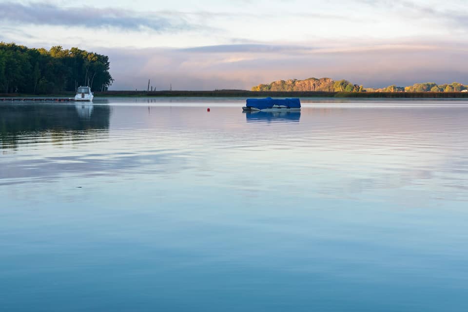 A calm lake with a boat and a covered structure on the shore.