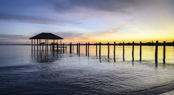 A pier extending into calm waters with a thatched-roof structure at the end.