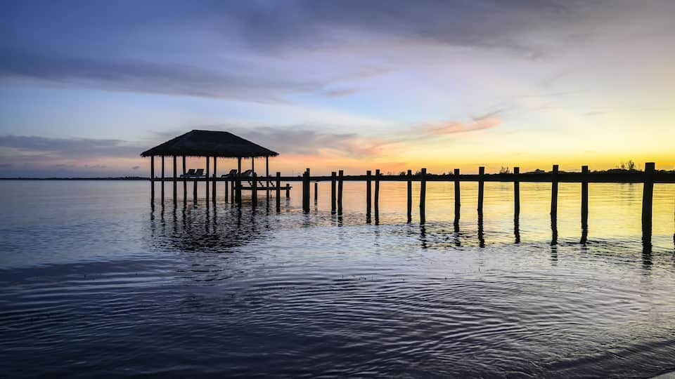 Un muelle se adentra en aguas tranquilas, con una estructura de techo de paja al final.