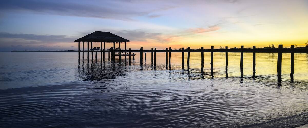 A pier extending into calm waters with a thatched-roof structure at the end.
