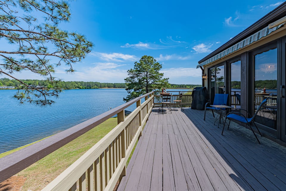 Una terraza de madera con vista a un lago, bajo un cielo despejado.