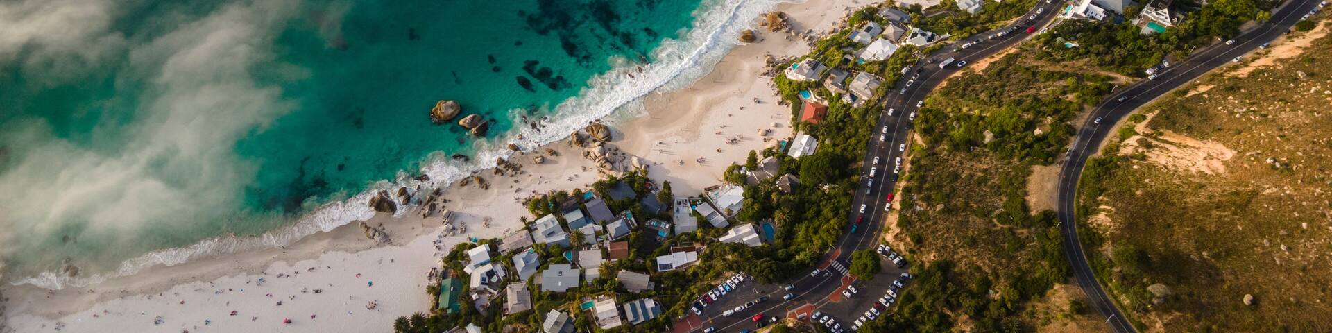 Vista aérea de un pueblo costero con playa, aguas azules cristalinas y carreteras sinuosas.