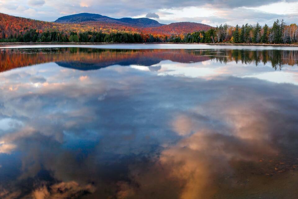 A calm lake reflecting autumn trees and mountains.