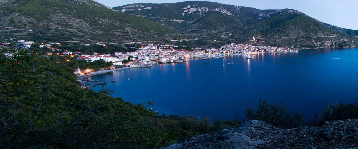 A coastal town with a harbor, surrounded by mountains and dense greenery.