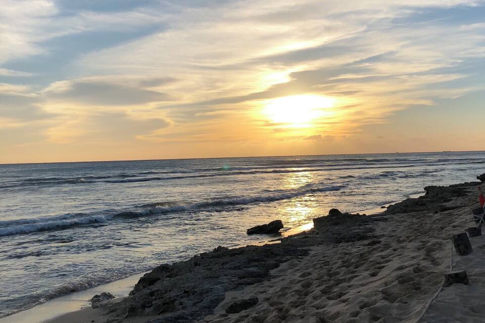 A beach at sunset with waves, a rope barrier, and a clear sky.