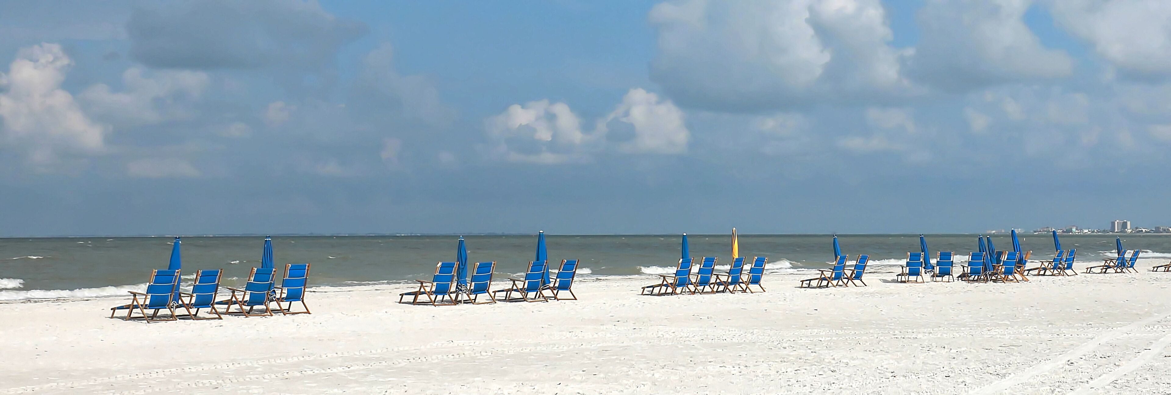 Panoramic view of beach chairs on the white sands of Fort Myers Beach facing the Gulf of Mexico.