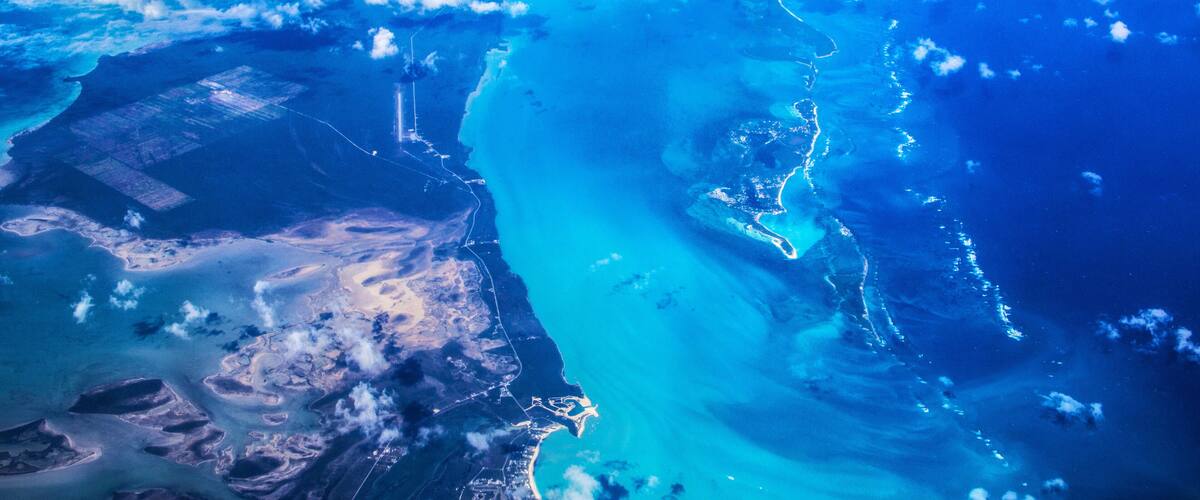 A coastal landscape with clear blue waters, sandy beaches, and scattered clouds.