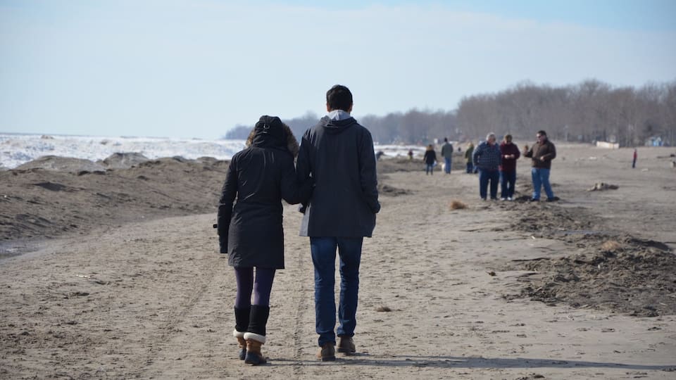 A sandy beach with people walking and standing in the distance.