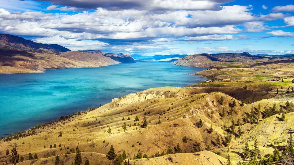A mountainous landscape with a large body of water, clear skies, and scattered trees.