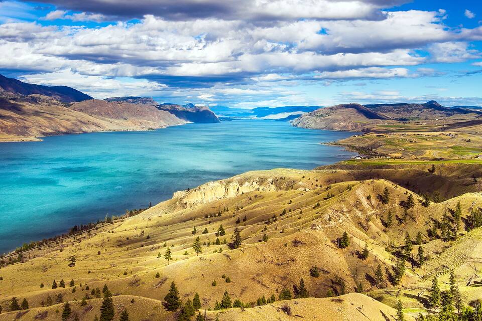 A mountainous landscape with a large body of water, clear skies, and scattered trees.