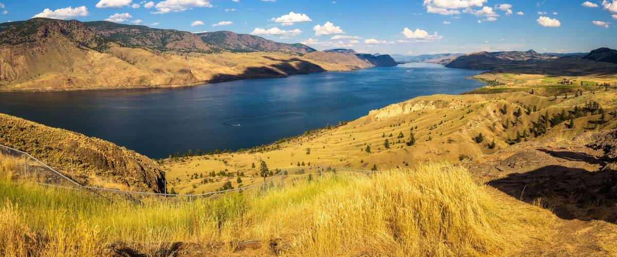 A large lake surrounded by rolling hills and mountains under a clear blue sky.