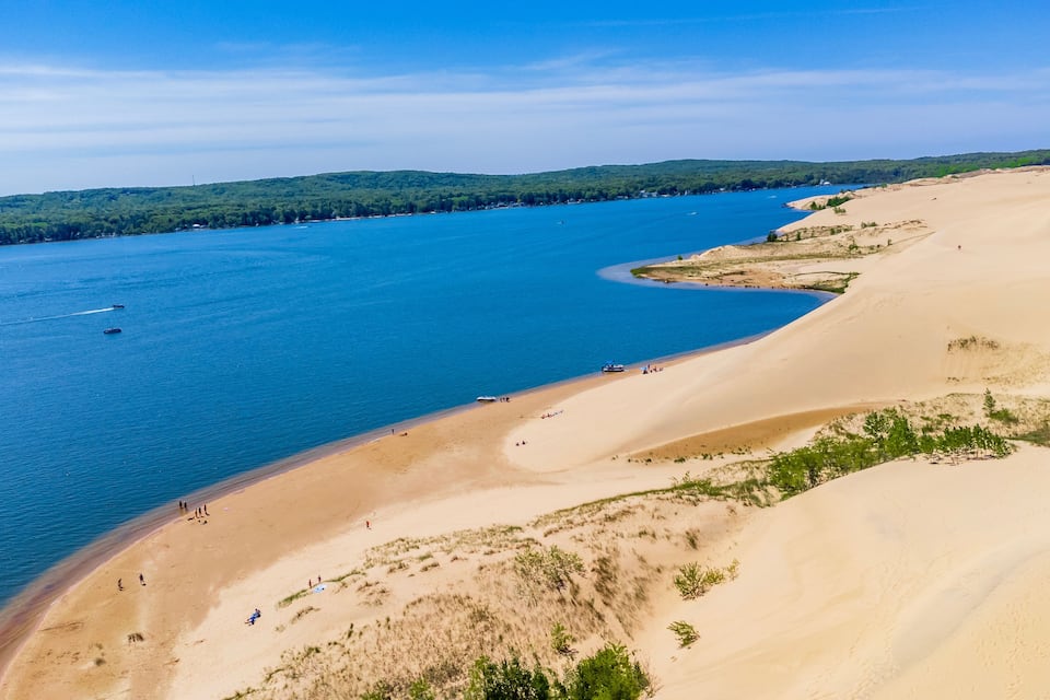 A coastal landscape with a sandy beach, a river, and a forested hill in the background.