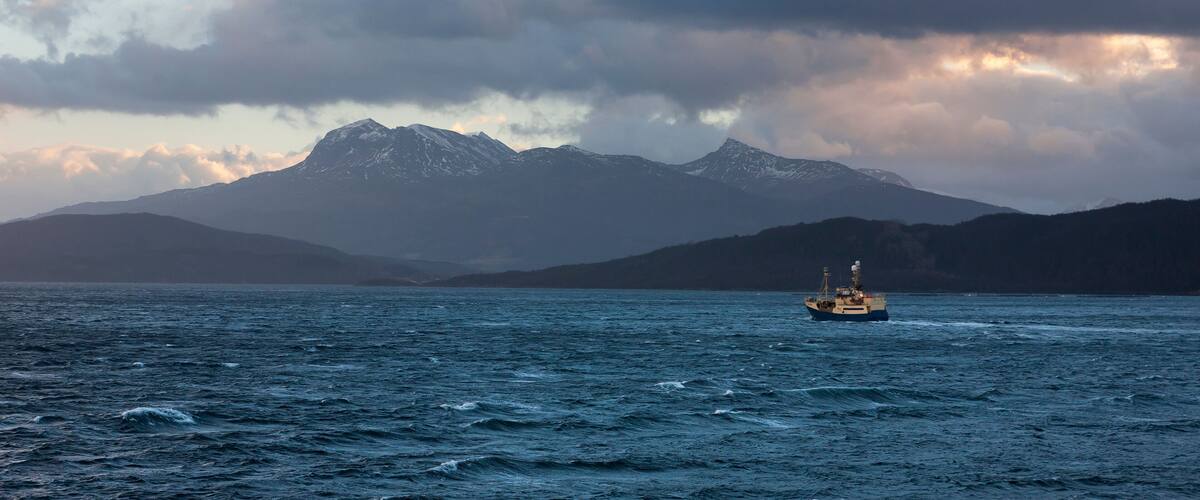 A boat on a calm sea with mountains in the background.