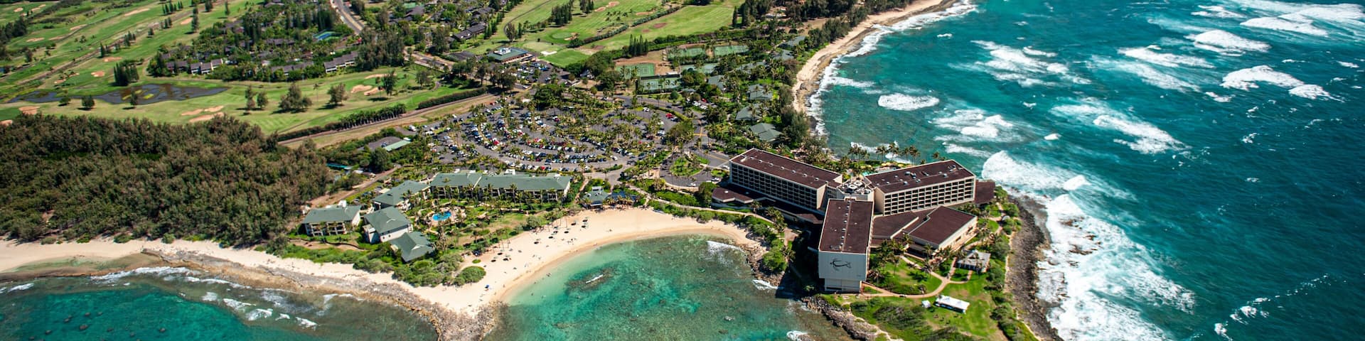 A coastal resort with a beach, ocean, and lush green hills.