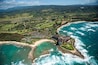 Un complejo turístico frente al mar con playa, océano y colinas verdes exuberantes.