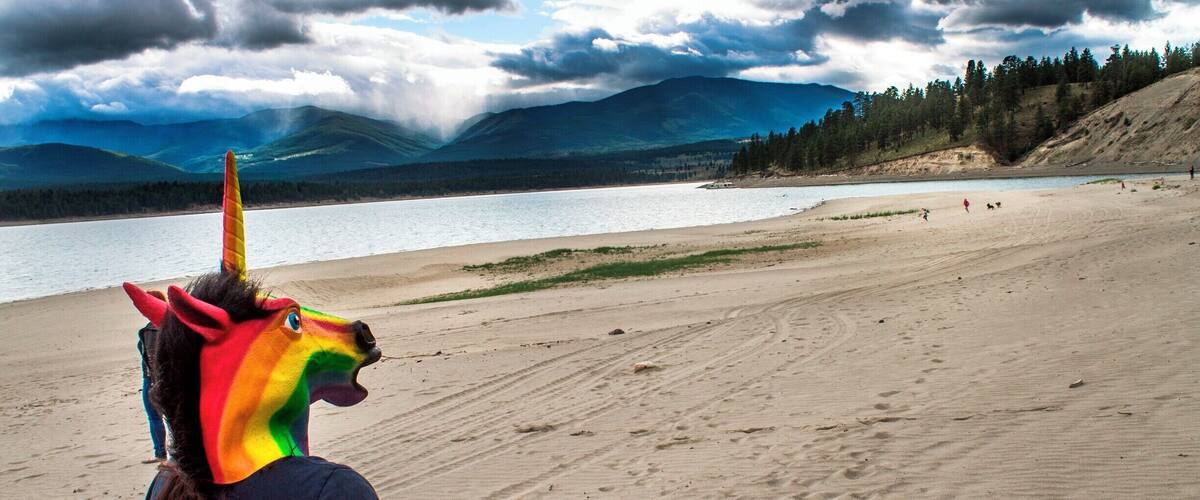 A beach with a lake, mountains, and a cloudy sky.
