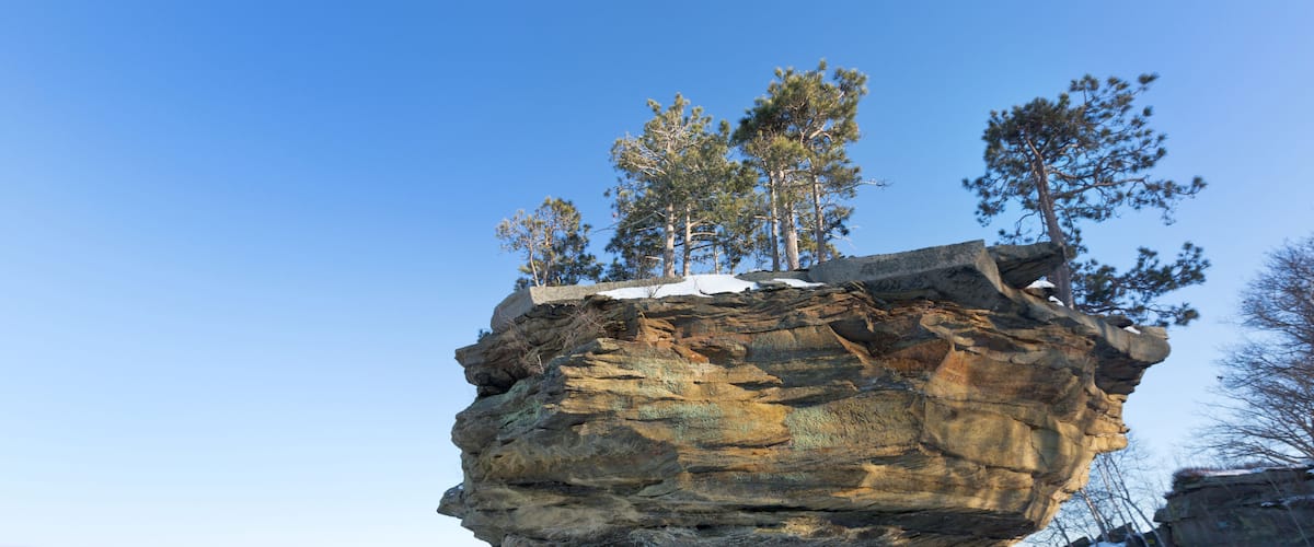 A rock formation with trees on top, surrounded by snow.