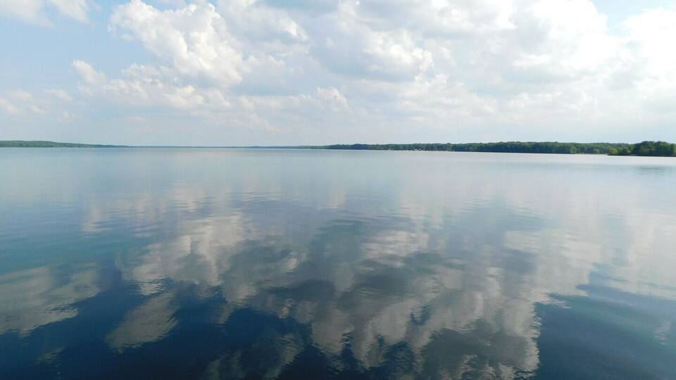 A calm lake with a clear reflection of the sky and clouds.