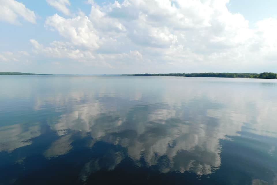 A calm lake with a clear reflection of the sky and clouds.