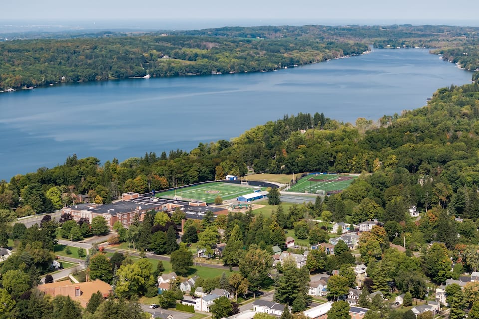 An aerial view of a residential area with a large lake, a football field, and surrounding greenery.