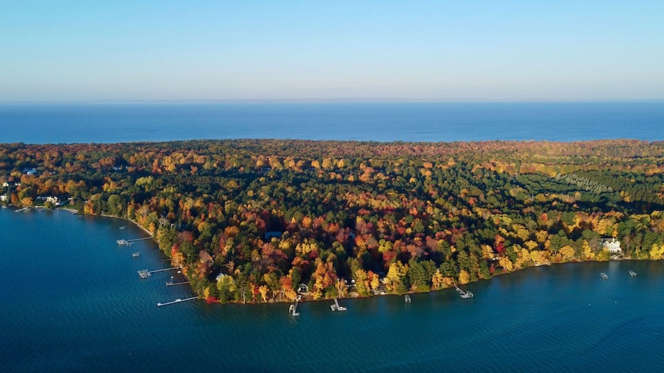 An aerial view of a lake surrounded by autumn-colored trees and a few houses.