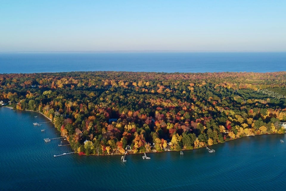 An aerial view of a lake surrounded by autumn-colored trees and a few houses.