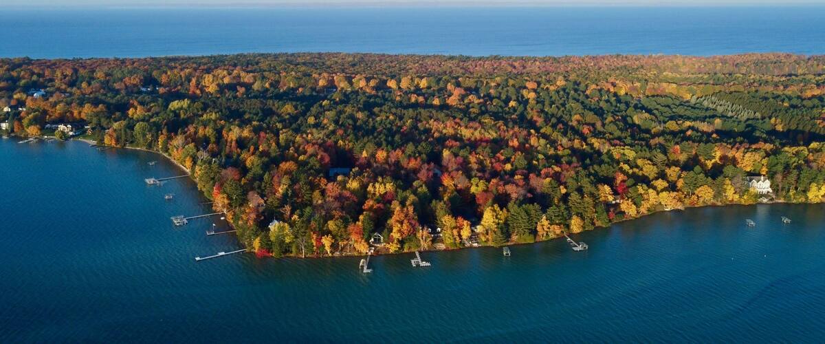 An aerial view of a lake surrounded by autumn-colored trees and a few houses.