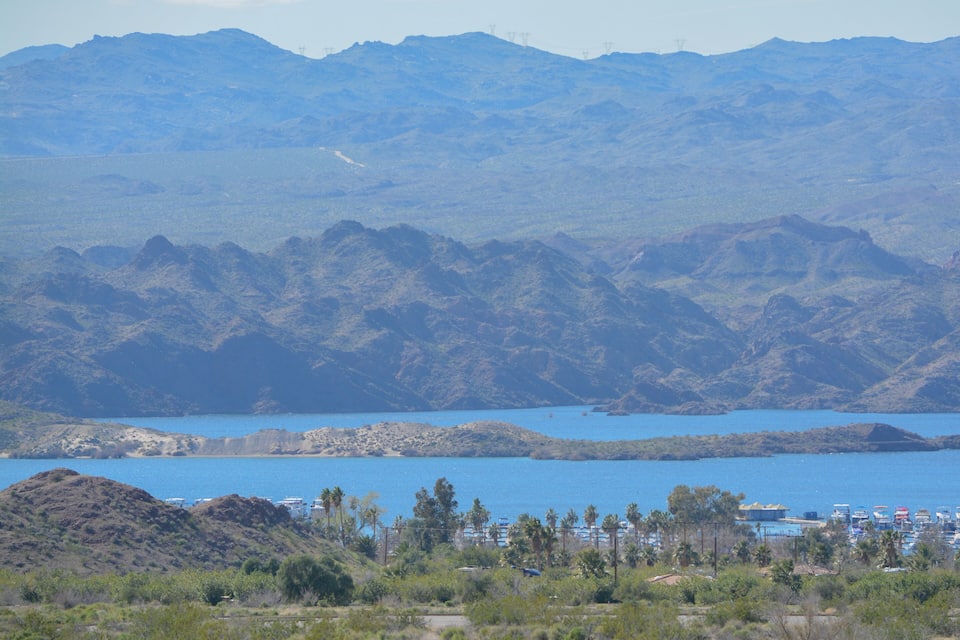 A coastal landscape with mountains, a body of water, and a marina with boats.