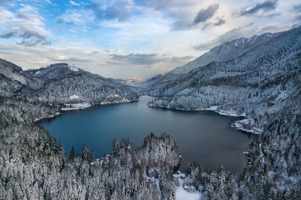 Um lago coberto de neve, ladeado por montanhas arborizadas.